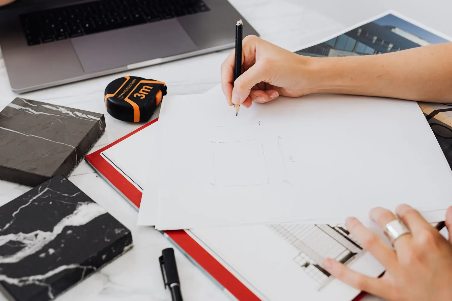 Hand sketching a kitchen cabinet layout with a tape measure and stone samples