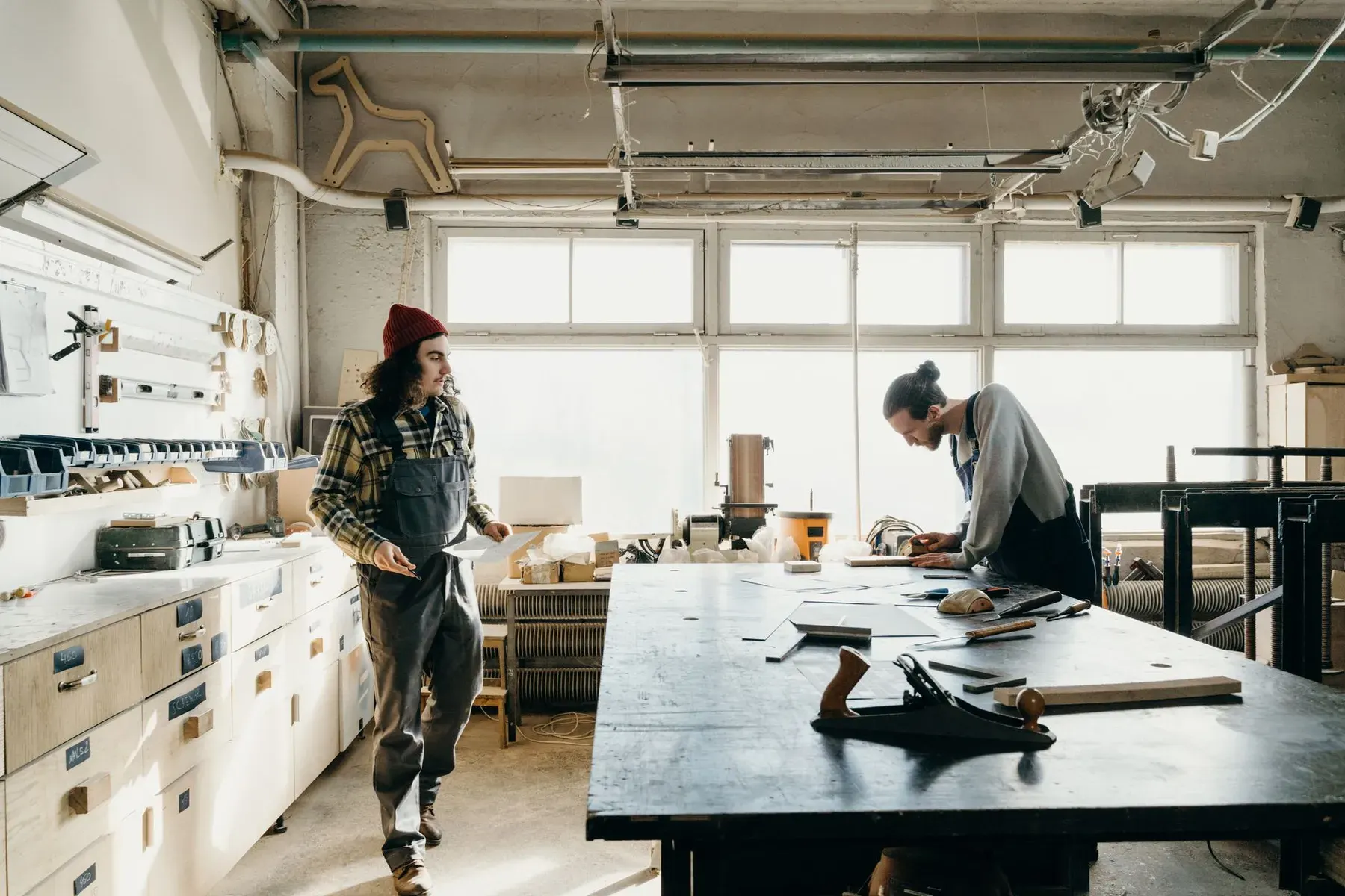 Woodworkers in a cabinet workshop with workbenches and a large window